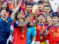 Radość reprezentacji Hiszpanii w piłce nożnej mężczyzn po zdobyciu pucharu. Piłkarze w złotych medalach i czerwonych koszulkach świętują z trofeum.