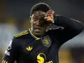 Młody piłkarz Kobbie Mainoo w czarnej koszulce Manchester United z żółtymi pasami, wyciera pot z czoła.