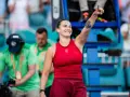 Uśmiechnięta Sabalenka w czerwonym stroju, z podniesionym palcem, jakby mówiła "tu gdzie mieszka Sabalenka!".