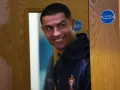 Uśmiechnięty Cristiano Ronaldo w granatowej bluzie z herbem Portugalii. Zastanawia się nad datami dołączenia do drużyny.