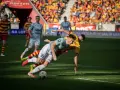 Zacięta walka na boisku podczas meczu Jagiellonia Białystok – Piast. Piłkarze walczą o piłkę, jeden z nich upada.