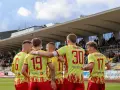Piłkarze Znicza Pruszków w żółtych koszulkach z czerwonymi detalami świętują na boisku. Ich determinacja i stalowa wola walki są widoczne.