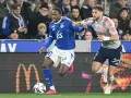 Piłkarz RC Strasbourg w niebieskiej koszulce z numerem 20 walczy o piłkę z zawodnikiem Olympique Lyon.