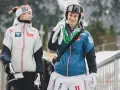 Dwóch zawodników mś skoki narciarskie, młoda kobieta w białej kurtce i mężczyzna w niebieskiej, niosący narty.