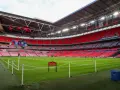 Pusta trybuna stadionu Wembley, który jest największym stadionem na świecie, z zieloną murawą i czerwonymi siedzeniami.