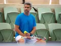 Tomasz Wiktorowski, trener Igi Świątek, siedzi na trybunach z rakietą i piłką tenisową, czekając na kolejny mecz.