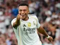 Uśmiechnięty Kylian Mbappé w białej koszulce Realu Madryt wskazuje palcem na widza, celebrując zwycięstwo.