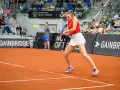 Sofia Żuk w akcji na korcie tenisowym, w czerwonej koszulce i białej spódniczce, gotowa do uderzenia.