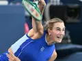 Aryna Sabalenka w akcji, z rakietą w górze, gotowa do serwisu. Widać jej skupienie i determinację, kiedy gra Sabalenka.