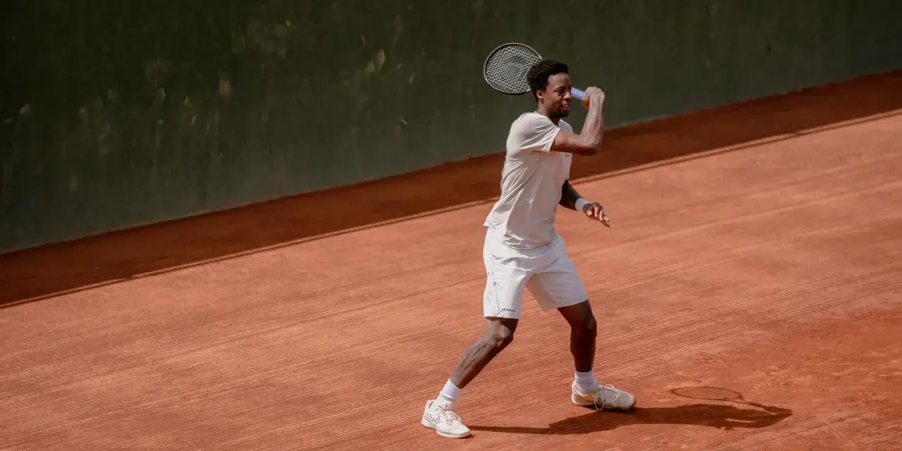 Tenisista w akcji na korcie ziemnym, celując w klasyczny wielki szlem.