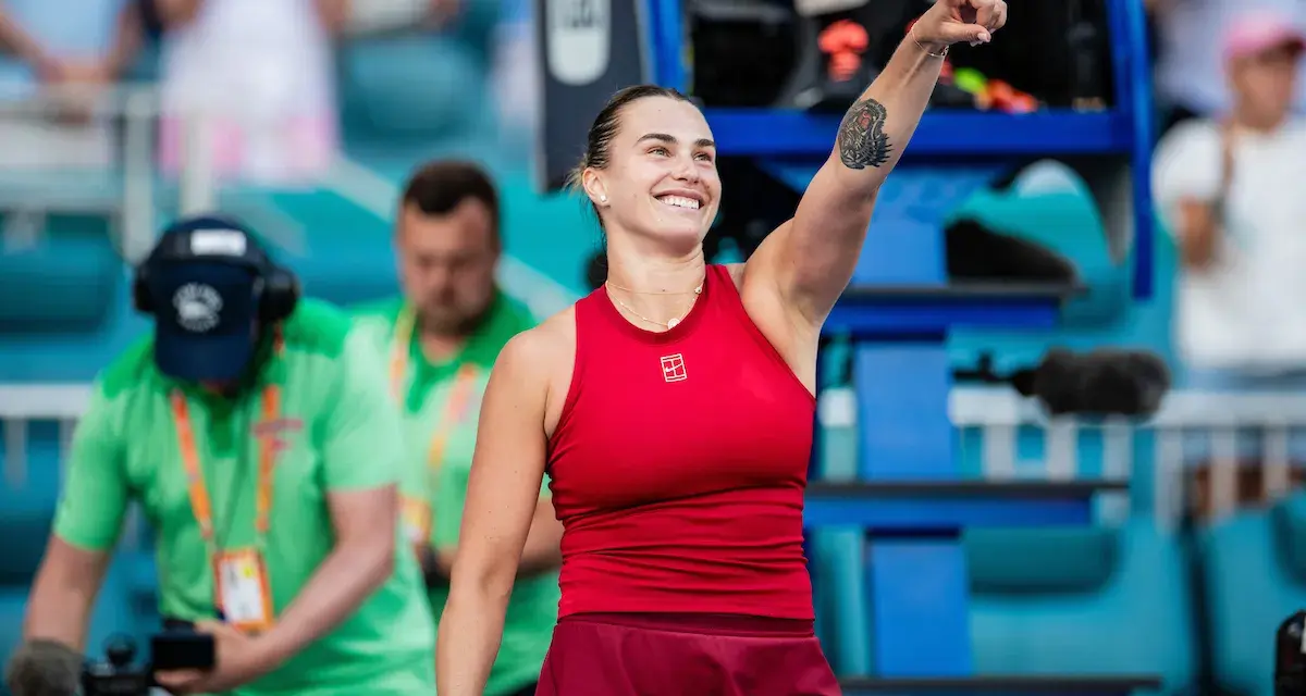 Uśmiechnięta Sabalenka w czerwonym stroju, z podniesionym palcem, jakby mówiła "tu gdzie mieszka Sabalenka!".