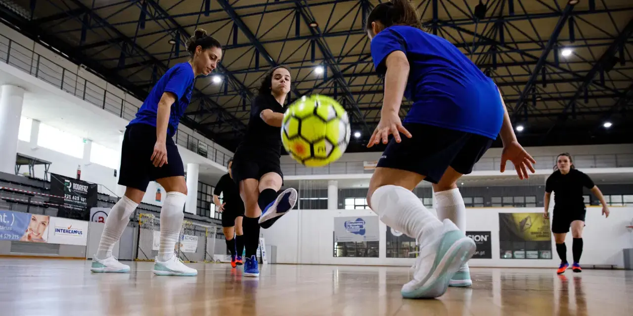 Graczki w hali sportowej ćwiczą zagrania, jedna z nich wykonuje pivot, podając piłkę nożną.