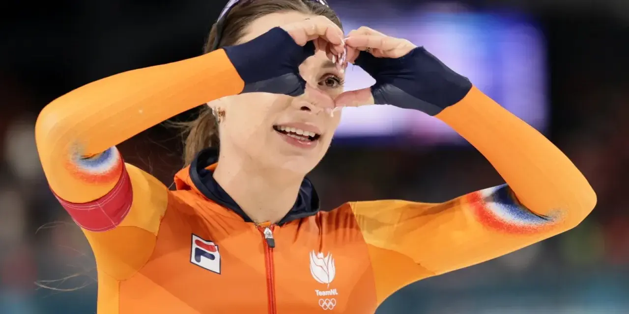 Femke Kok w pomarańczowym stroju TeamNL tworzy serce dłońmi, patrząc przez nie z uśmiechem.