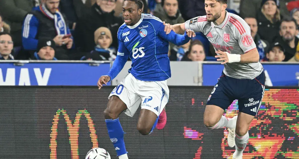 Piłkarz RC Strasbourg w niebieskiej koszulce z numerem 20 walczy o piłkę z zawodnikiem Olympique Lyon.