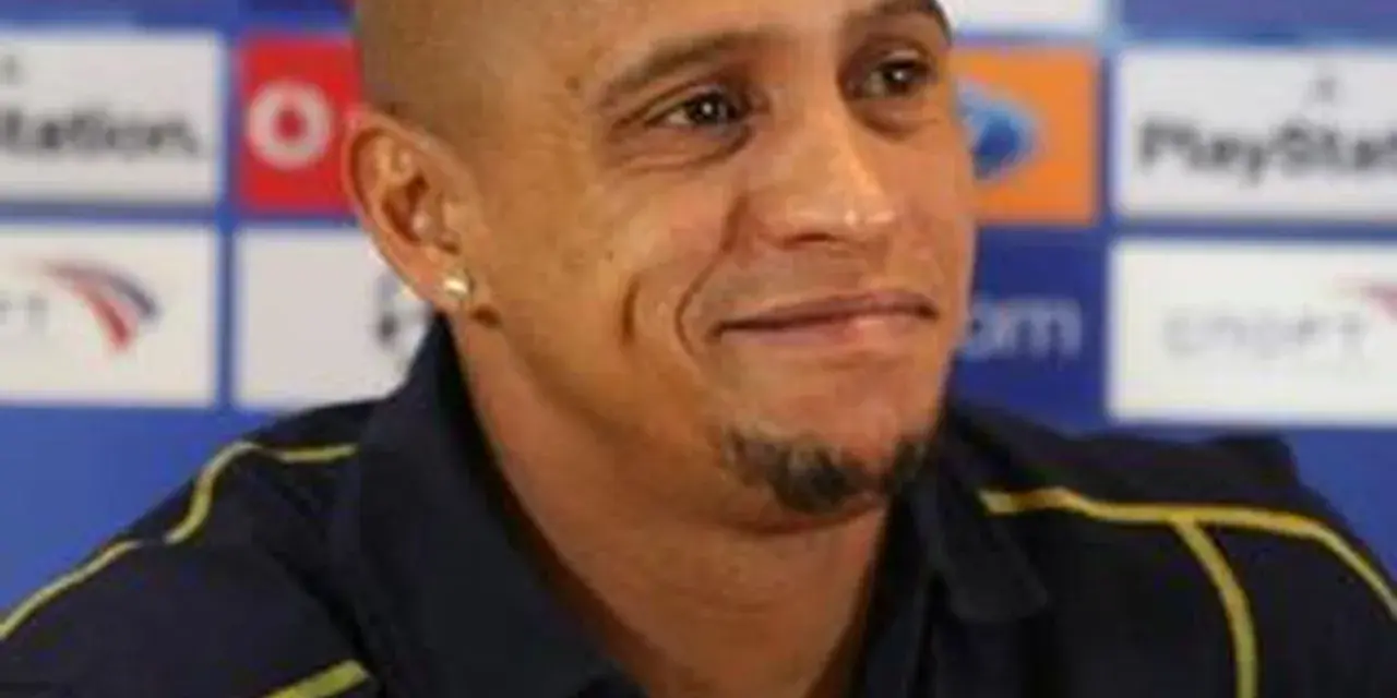 Roberto Carlos, znany z prowadzenia drużyn, w ciemnej koszulce z żółtymi akcentami, na tle z logo PlayStation.
