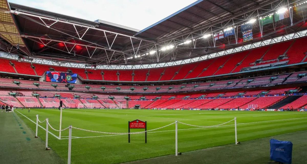 Pusta trybuna stadionu Wembley, który jest największym stadionem na świecie, z zieloną murawą i czerwonymi siedzeniami.