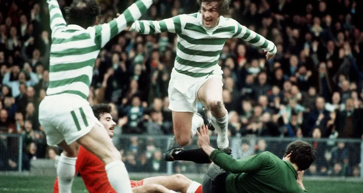 Futboliści z Glasgow w zielono-białych pasach świętują zwycięstwo, jeden z nich przeskakuje nad leżącym przeciwnikiem.
