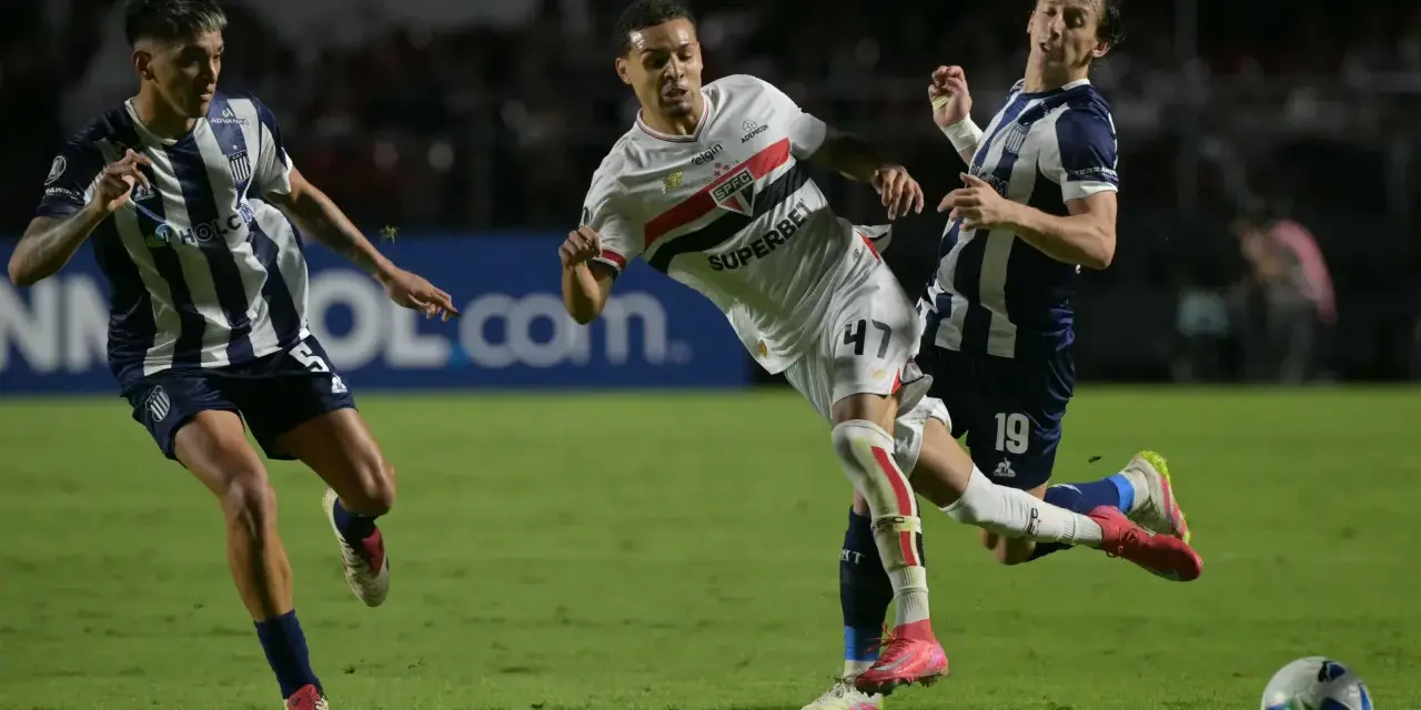 Piłkarze walczą o piłkę na boisku, jeden z nich w białej koszulce z logo São Paulo FC, walcząc o wysokie rankingi.