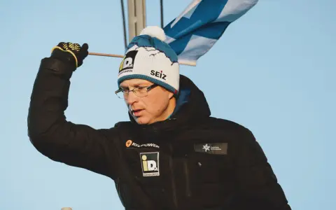 Igor Medved w czapce z pomponem i flagą Finlandii, w czarnej kurtce z logo.