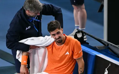 Tenisista z pomarańczową opaską na przedramieniu podczas Australian Open 2024 otrzymuje pomoc od fizjoterapeuty.