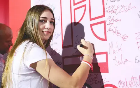Julia Szeremeta pisze swoje imię na białej ścianie z czerwonymi elementami.