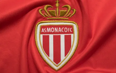 Herb AS Monaco FC na czerwonym tle. Duma z osiągnięć i rankingi klubu.