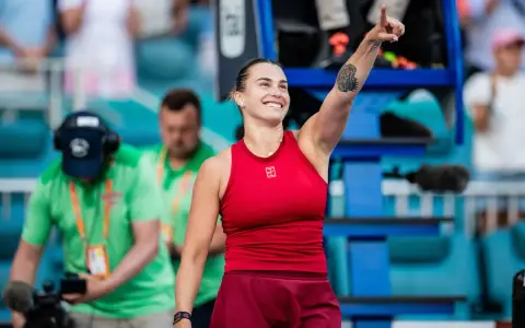 Uśmiechnięta Sabalenka w czerwonym stroju, z podniesionym palcem, jakby mówiła "tu gdzie mieszka Sabalenka!".
