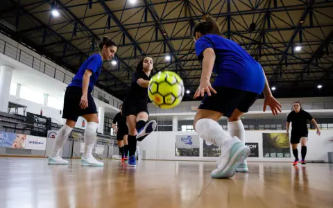 Graczki w hali sportowej ćwiczą zagrania, jedna z nich wykonuje pivot, podając piłkę nożną.