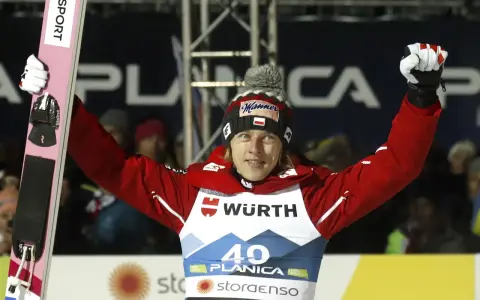 Skoczek narciarski w czerwonej kurtce i czapce z polską flagą świętuje zwycięstwo na skoczni. Mistrzostwa świata w skokach narciarskich.