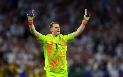Manuel Neuer, bramkarz w neonowożółtej koszulce z numerem 1, świętuje zwycięstwo, unosząc ręce w geście triumfu.