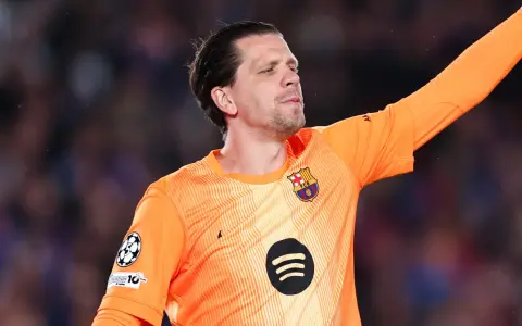 Wojciech Szczęsny w pomarańczowej koszulce bramkarskiej FC Barcelony, z podniesioną ręką, gotowy do obrony.