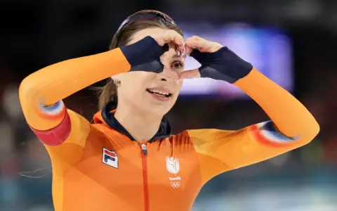 Femke Kok w pomarańczowym stroju TeamNL tworzy serce dłońmi, patrząc przez nie z uśmiechem.