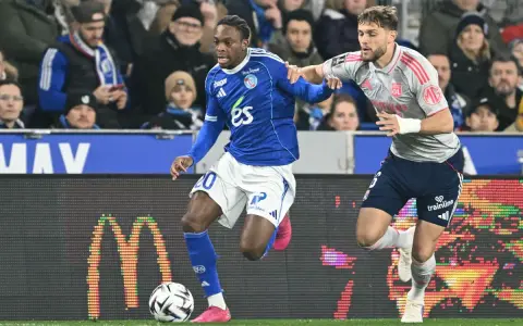 Piłkarz RC Strasbourg w niebieskiej koszulce z numerem 20 walczy o piłkę z zawodnikiem Olympique Lyon.