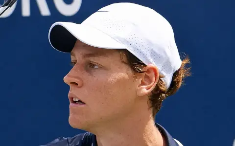 Jannik Sinner w białej czapce z daszkiem, skupiony na grze.