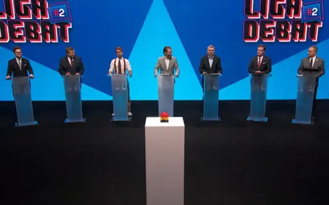 Siedmiu mężczyzn w garniturach stoi za mównicami. W tle logo "Liga Debat #2".