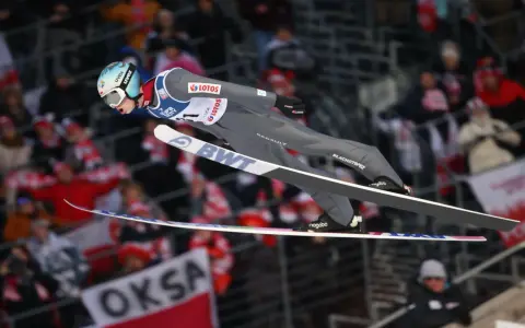 Skoki narciarskie dzisiaj: polski skoczek w locie, tłum kibiców na trybunach.