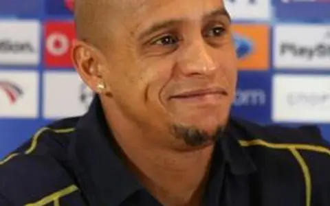 Roberto Carlos, znany z prowadzenia drużyn, w ciemnej koszulce z żółtymi akcentami, na tle z logo PlayStation.