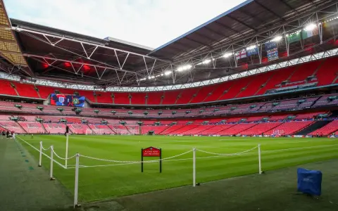 Pusta trybuna stadionu Wembley, który jest największym stadionem na świecie, z zieloną murawą i czerwonymi siedzeniami.