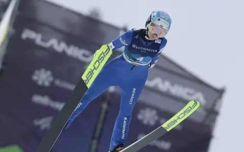 Skoczkini narciarska w locie, w niebieskim kombinezonie, z nartami Fischer. Planica.