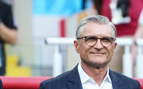 Uśmiechnięty mężczyzna w okularach, były trener reprezentacji Polski, w garniturze i białej koszuli.
