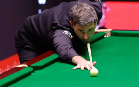 Ronnie O'Sullivan, jeden z najlepsi snookerzyści wszechczasów, skupiony przy zielonym suknie, celuje w bilę.