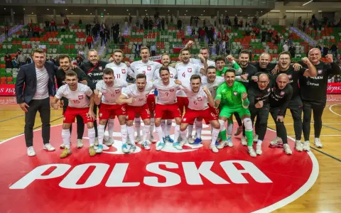 Drużyna Polski świętuje sukces na futsalowych mistrzostwach świata. Piłkarze w biało-czerwonych strojach z dumą pozują na tle napisu "POLSKA".