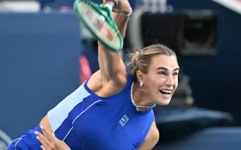 Aryna Sabalenka w akcji, z rakietą w górze, gotowa do serwisu. Widać jej skupienie i determinację, kiedy gra Sabalenka.