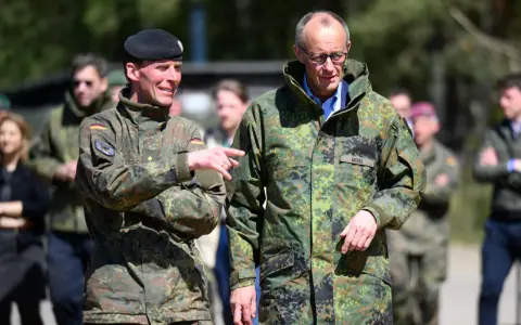 Dwóch mężczyzn w mundurach wojskowych, jeden z flagą Polski, drugi z napisem "MERZ" (Niemcy).