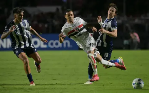 Piłkarze walczą o piłkę na boisku, jeden z nich w białej koszulce z logo São Paulo FC, walcząc o wysokie rankingi.