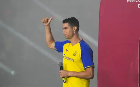 Cristiano Ronaldo w koszulce Al Nassr z mikrofonem, pokazuje kciuk w górę.