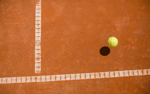 Piłka tenisowa na ceglanej nawierzchni, tuż obok linii bocznej. Czy to decydujący punkt za Roland Garros?