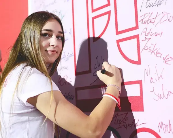 Julia Szeremeta pisze swoje imię na białej ścianie z czerwonymi elementami.