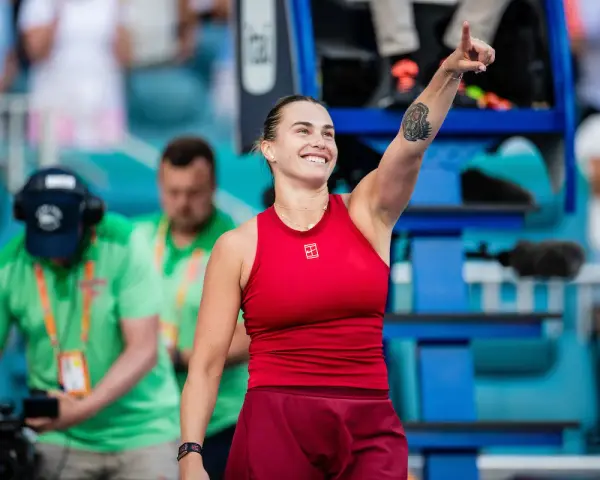 Uśmiechnięta Sabalenka w czerwonym stroju, z podniesionym palcem, jakby mówiła "tu gdzie mieszka Sabalenka!".