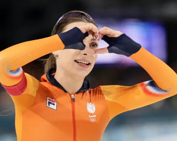 Femke Kok w pomarańczowym stroju TeamNL tworzy serce dłońmi, patrząc przez nie z uśmiechem.
